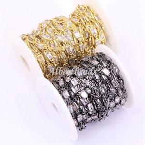 Puede incluir: Dos carretes de cadena con cristales transparentes de forma cuadrada. Un carrete tiene una cadena dorada y el otro una cadena negra.