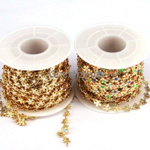 May include: Two spools of gold-colored chain trim with flower-shaped links. One spool has white flower centers, the other has colorful centers.