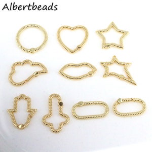 May include: Assortment of gold-toned metal charms in various shapes, including a heart, star, cloud, lips, and a hand-shaped charm. The charms are all connected with a small metal ring.