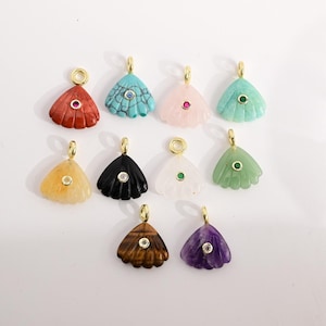 Op de afbeelding: Een verzameling edelsteenhangers in verschillende kleuren, waaronder rood, turquoise, roze en groen. Elke hanger heeft een waaiervorm met een goudkleurige beugel en een kleine edelsteen of kristallen accent in het midden. De hangers worden tegen een witte achtergrond getoond.