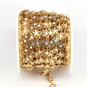 May include: Gold chain trim with small white flower-shaped links. The chain is wound around a white spool.