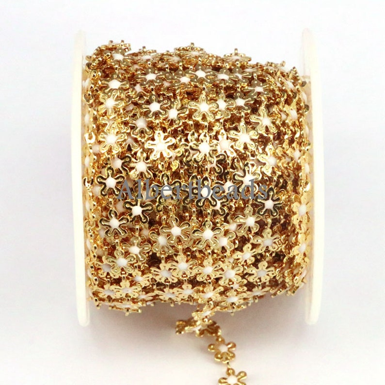 May include: Gold chain trim with small white flower-shaped links. The chain is wound around a white spool.