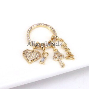 Op de afbeelding: Gouden charmbracelet met een hart-, sleutel- en "Love"-bedel. Elke bedel is versierd met heldere zirkonia-stenen.