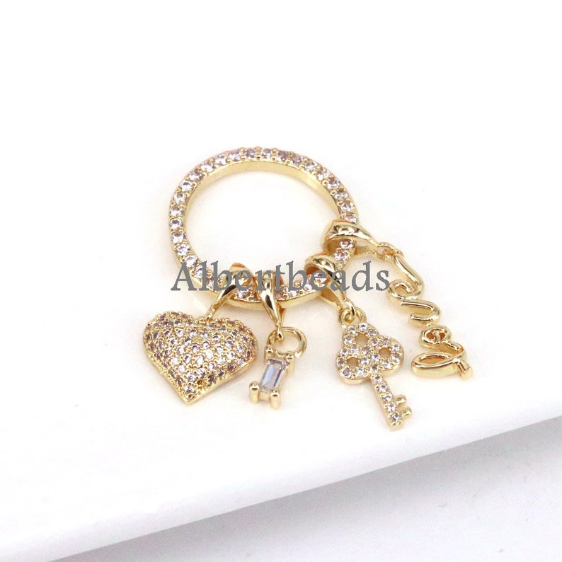 Op de afbeelding: Gouden charmbracelet met een hart-, sleutel- en "Love"-bedel. Elke bedel is versierd met heldere zirkonia-stenen.