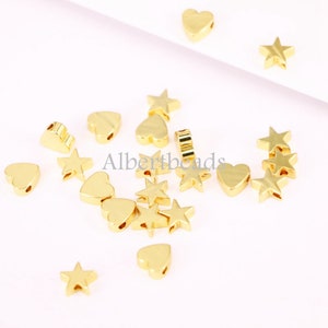 May include: A collection of gold-toned metal charms in the shapes of stars and hearts. The charms have a hole in the centre for stringing on jewellery.
