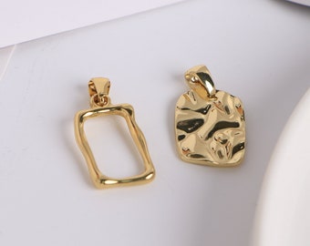 May include: Two gold-coloured pendants. One is a rectangular frame, the other is a textured, solid rectangle. Both have a small loop at the top for a chain. The pendants are on a white surface.