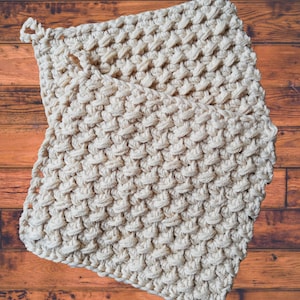 May include: A cream-colored crocheted dishcloth with a textured pattern. The dishcloth is folded in half and has a loop at the top for hanging.
