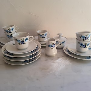 Könnte beinhalten: Ein Vintage-Teeservice aus weißem Porzellan mit blauem Blumenmuster. Das Set umfasst Tassen, Untertassen, Teller, einen Sahnekännchen und eine Zuckerdose. Die Tassen und das Sahnekännchen haben Henkel.