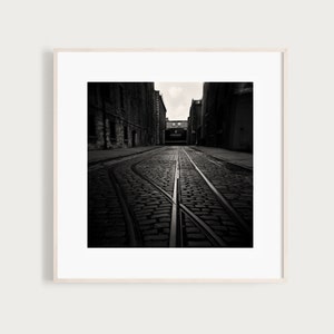 May include: A black and white photograph of a cobblestone street with train tracks leading to a building with the word "GUINNESS" on it.