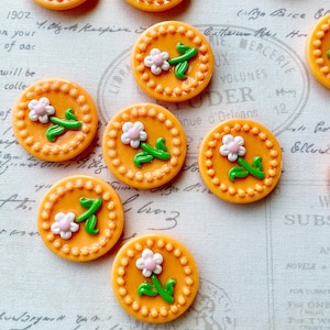 May include: Nine orange and white floral buttons with a green stem and leaves. The buttons have a beaded edge.