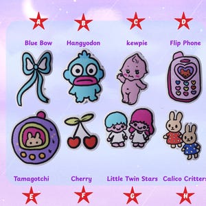 May include: A collection of colorful cartoon stickers featuring a blue bow, Hangyodon, kewpie, a flip phone, Tamagotchi, cherries, Little Twin Stars, and Calico Critters. The stickers are arranged on a light purple background.