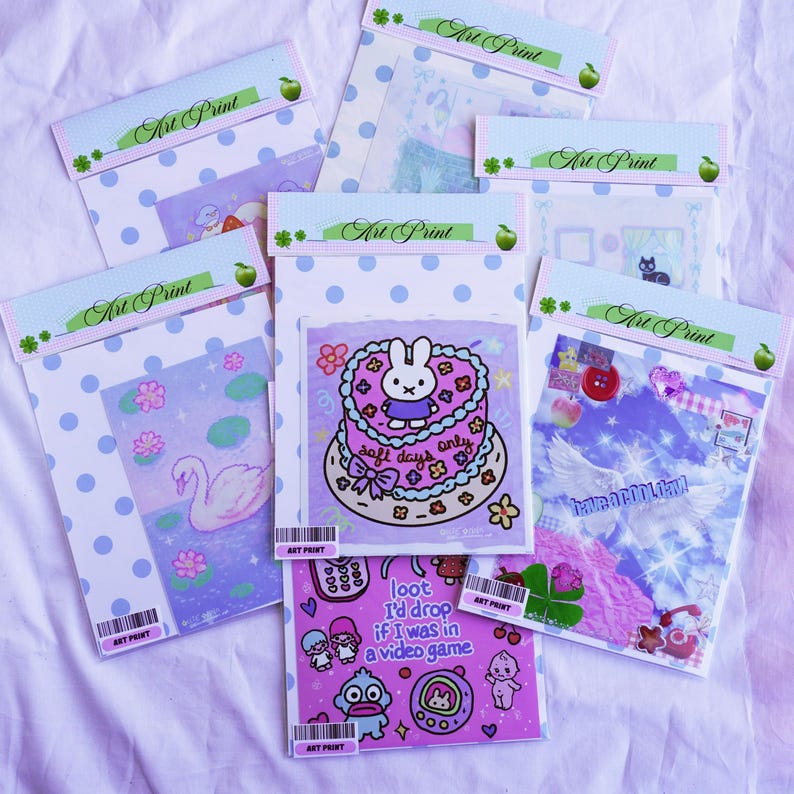 May include: A collection of art prints in clear plastic sleeves, each with a unique design. The prints feature illustrations of a swan, a cake with a bunny, and other cute graphics. The packaging includes the text "Art Print".