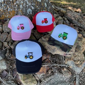May include: Four trucker hats with different colored brims and a white mesh back. Each hat features an embroidered tractor design in a different color: pink, red, green, and blue.