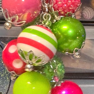 May include: A cluster of colorful, decorative charms. The charms include a variety of round beads in bright pink, green, and red, some with stripes or polka dots. The beads are connected with silver-colored chains and accents.
