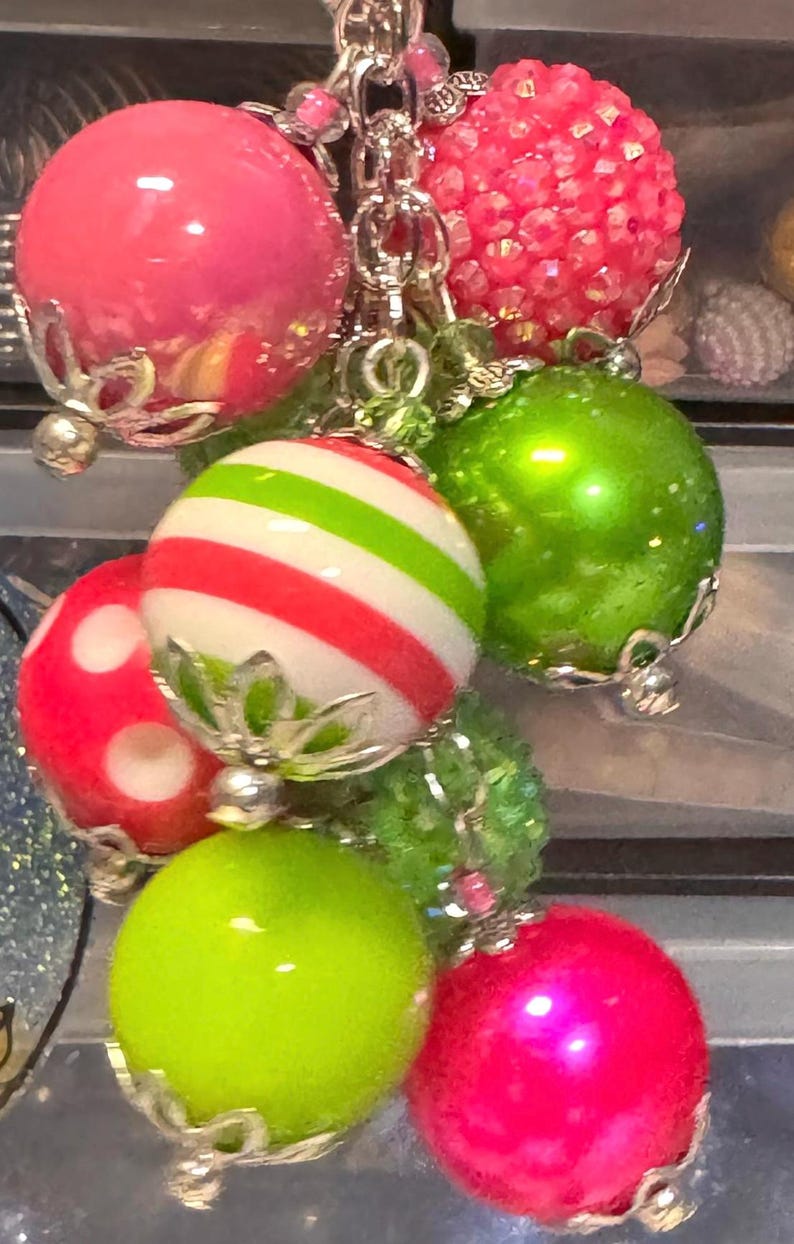 May include: A cluster of colorful, decorative charms. The charms include a variety of round beads in bright pink, green, and red, some with stripes or polka dots. The beads are connected with silver-colored chains and accents.