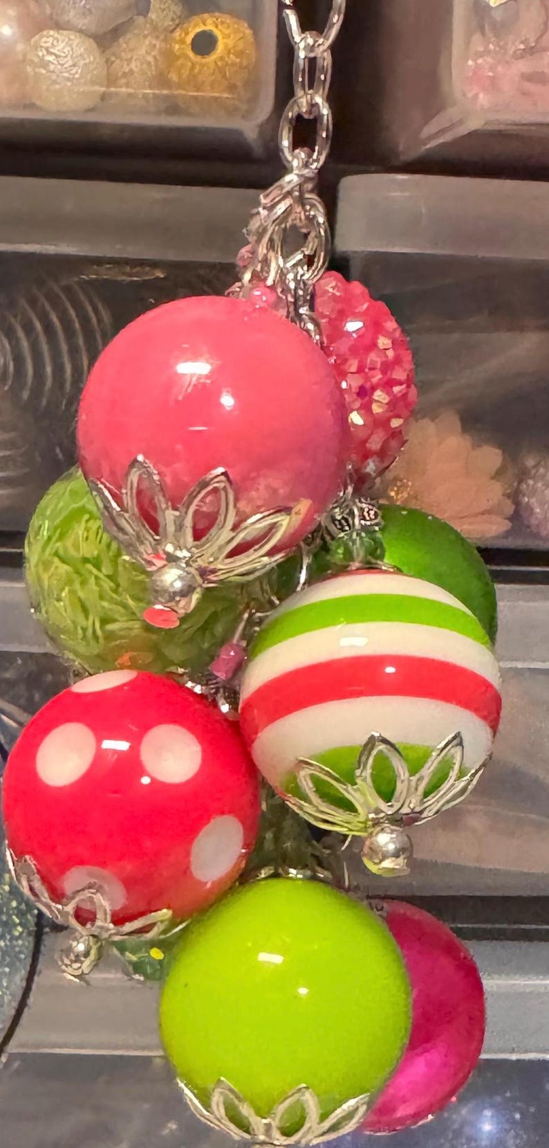 May include: A cluster of colorful, decorative ornaments. The ornaments are various colors, including pink, green, and red, with silver-colored metal accents. Some have stripes or polka dots.