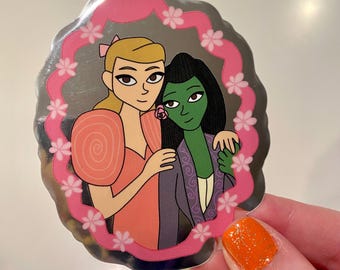 Peut inclure: Un autocollant représentant deux femmes de dessin animé s'embrassant, encadrées par une bordure florale rose. L'une a les cheveux blonds et porte une robe pêche, l'autre a la peau verte et les cheveux noirs, vêtue d'une tenue violette. L'autocollant a un fond métallique argenté.