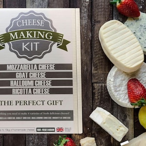 May include: A cheese-making kit box with text, surrounded by various cheeses, strawberries, and a pear on a wooden surface. The box reads "Cheese Making Kit" and lists mozzarella, goat, halloumi, and ricotta cheeses.
