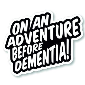 May include: A white sticker with a black border featuring the phrase "ON AN ADVENTURE BEFORE DEMENTIA!" in a bold, playful font. The sticker has a subtle shadow effect, creating a 3D look. The design is simple and striking.