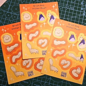 May include: Three orange sticker sheets with the text "Brush Bug Sticker Sheet" and illustrations of cartoon bugs. The stickers feature various bug designs in white, tan, and purple, with a sparkling star background.