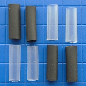 May include: Eight heat shrink tubing pieces, four black and four clear, arranged in two rows of four on a blue grid background.