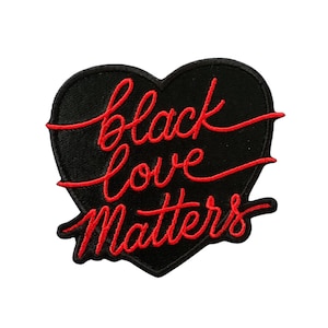 May include: Black heart-shaped patch with the words "black love matters" embroidered in red script. The patch has a black border and is likely made of fabric. The design is simple and bold.