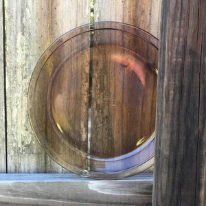 Puede incluir: Un plato para tartas de vidrio transparente con un tono marrón. El plato está sobre una superficie de madera.