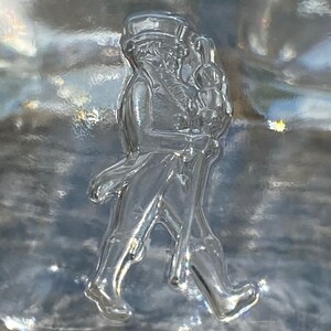 May include: A clear glass bottle with a raised design of a man in a top hat and coat walking with a cane.