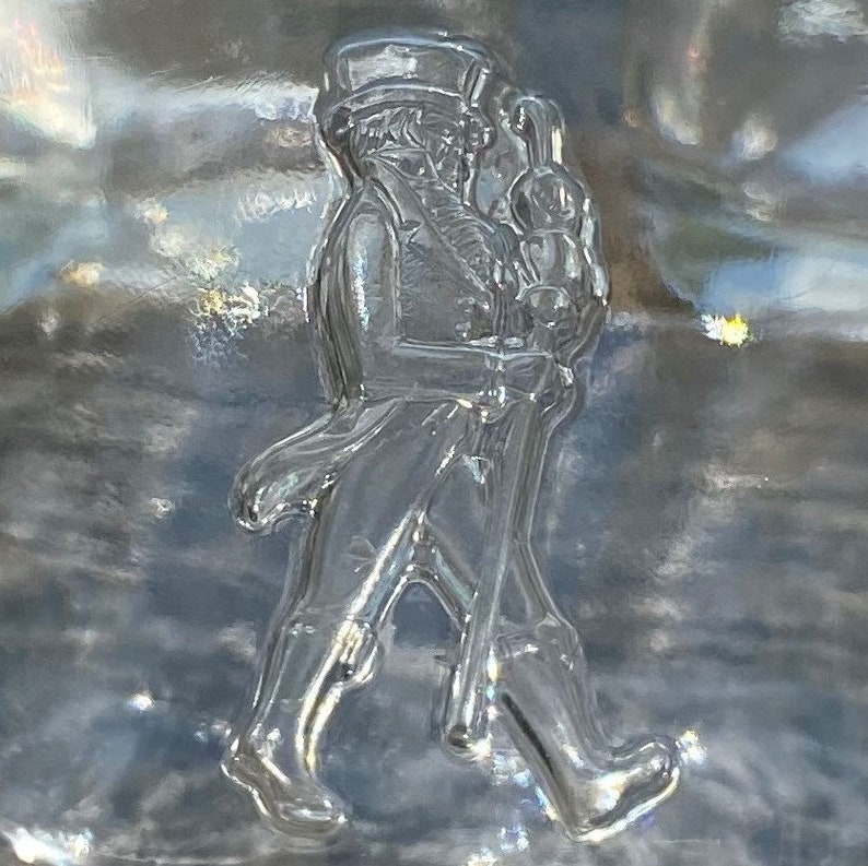 May include: A clear glass bottle with a raised design of a man in a top hat and coat walking with a cane.