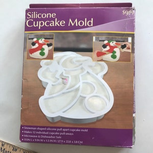 May include: A purple box with a white silicone snowman-shaped cupcake mold. The box reads "Silicone Cupcake Mold" and shows images of the finished cupcakes. The mold measures 11 inches long, 9 inches wide, and 1.5 inches high.