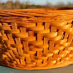 May include: A woven basket with a rounded shape and a natural, light brown color. The basket is made of interwoven strips of material, creating a textured surface. The basket is likely used for storage or display.
