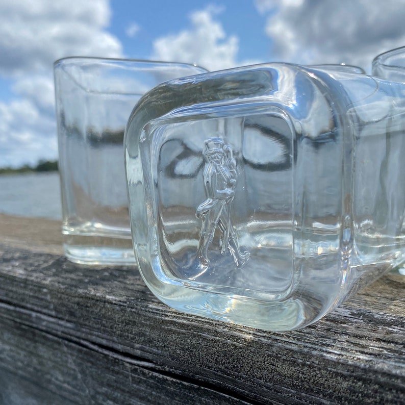 May include: Three clear glass tumblers with a square base and a raised square design on the front. The design features a raised image of a person in a military uniform.