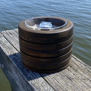 May include: A dark brown wooden ring holder with a clear glass insert. The holder is made of stacked rings of wood and has a smooth, polished finish.