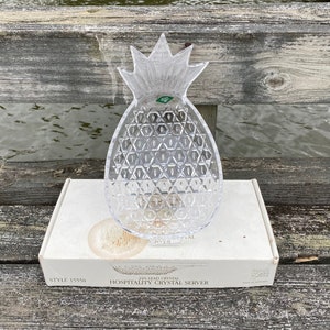 Könnte beinhalten: Klarer Kristall-Ananas-förmiger Servierer mit strukturierter Oberfläche. Der Servierer steht auf einer weißen Schachtel mit dem Text "24% Lead Crystal Hospitality Crystal Server". Er hat einen grünen Aufkleber.