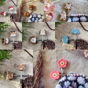 May include: A set of colourful animal and flower stitch markers for knitting and crocheting. The markers are attached to a metal needle with a T-shaped end. The markers are made of silicone and feature a variety of designs, including a deer, a dog, a cat, a mushroom, a flower, and a whale.