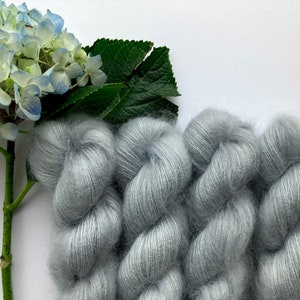 May include: Three skeins of soft, light blue yarn with a fuzzy texture. The yarn is arranged in a loose, spiral shape.