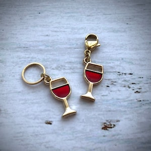 May include: Two gold-tone wine glass charms with red and white enamel. The charms are attached to a gold-tone ring and a lobster clasp.