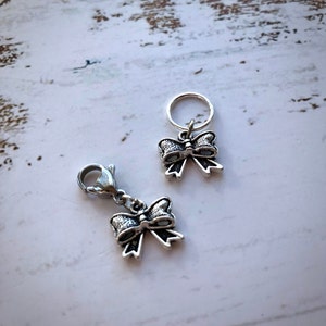 May include: Two silver bow-shaped stitch markers. One marker has a clasp and the other has a loop.