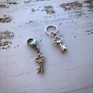 May include: Two silver key-shaped stitch markers. One marker has a silver lobster clasp and the other has a silver ring.