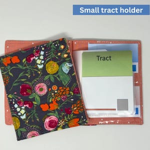 Puede incluir: Pequeño portafolletos abierto con una cubierta estampada floral en gris oscuro, rosa, naranja y amarillo. El interior tiene bolsillos transparentes y una tarjeta verde con la palabra "Tracto".