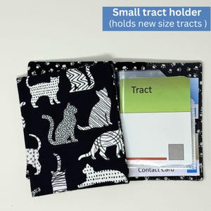 May include: A small, open tract holder featuring a black and white cat design. Inside, there's a clear plastic sleeve holding a green and white tract and a contact card. The text "Small tract holder" is displayed at the top.