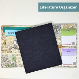 May include: A literature organizer with a map design. The organizer has a dark blue cover and several pockets and slots for papers and pens. The text "Literature Organizer" is at the top.