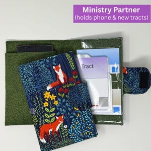 May include: A fabric ministry partner organizer featuring a dark blue exterior with a fox and floral pattern, a green interior, a black smartphone pocket, and clear plastic sleeves holding paper tracts, secured by a hook-and-loop fastener tab.