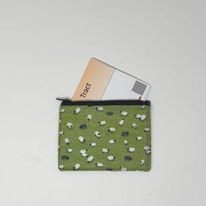 May include: A small, green zippered pouch with a pattern of white and gray sheep. A card with the word "Tract" is partially visible inside the pouch. The background is plain white.