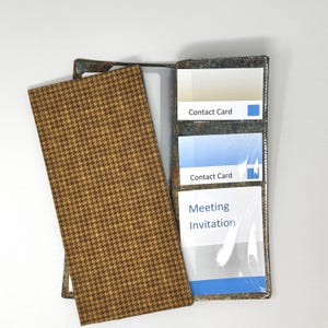 May include: A rectangular organizer wallet featuring a brown and tan houndstooth pattern on the exterior. The interior displays a mottled dark texture with three clear plastic slots containing cards labeled Contact Card and Meeting Invitation.