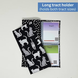May include: A black and white cat-themed long tract holder. The holder is open, revealing clear pockets with cards labeled "Tract." The cover features a repeating pattern of stylized cats. The text "Long tract holder (holds both tract sizes)" is in a blue rectangle.