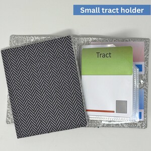 Puede incluir: Un pequeño portafolletos con una cubierta de patrón de espiga gris y blanco. El interior presenta un bolsillo transparente y una tarjeta verde con la palabra "Tract". El portafolletos está abierto, mostrando su contenido.