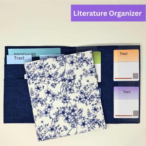 May include: A navy blue literature organizer with multiple pockets. The organizer features a floral patterned cover with blue flowers on a white background. The text "Literature Organizer" is in a purple rectangle at the top.
