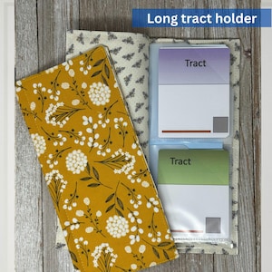 May include: A fabric long tract holder with a mustard yellow floral pattern. The holder is open, revealing clear plastic sleeves holding cards labeled "Tract." The holder is lined with a cream fabric with a bee pattern. The text "Long tract holder" is in a blue rectangle.