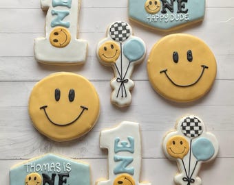 May include: Assortment of decorated sugar cookies with a smiley face theme. Includes cookies shaped like the number one, smiley faces, and balloons. Some cookies have the text "Thomas is One Happy Dude."